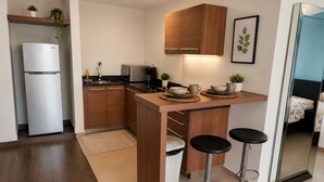 A compact kitchen with a refrigerator, microwave, and wooden cabinets. There are two stools and a small bar area.