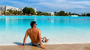 A man sitting by a clear blue pool with a resort in the background.