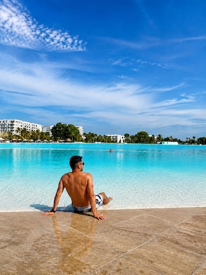 A man sitting by a clear blue pool with a resort in the background.