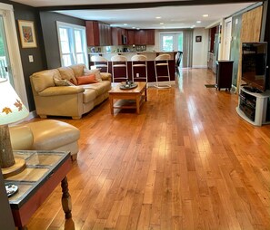 A spacious living room with a wooden floor, a sofa, a coffee table, and a television. - Under 500 dollars per night! Oversized 5BR & 4BA home in Meredith NH area! (New Hampton)