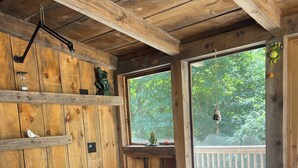 Un interno in legno con un tavolo rotondo e sedie, una finestra vista alberi e un balcone con ringhiera.