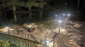 Un'area esterna illuminata di notte, con una scala in metallo, un braciere e un vialetto lastricato.