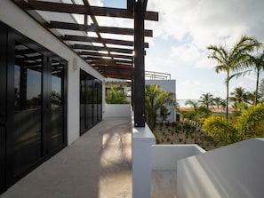 Un edificio moderno con un espacio exterior cubierto, grandes puertas de vidrio y vistas a una playa con palmeras.