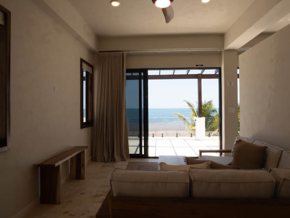A living room with a sofa, a bench, and a view of the beach through large glass doors.