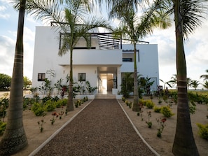 A modern building with a central entrance, surrounded by a gravel pathway and various plants.