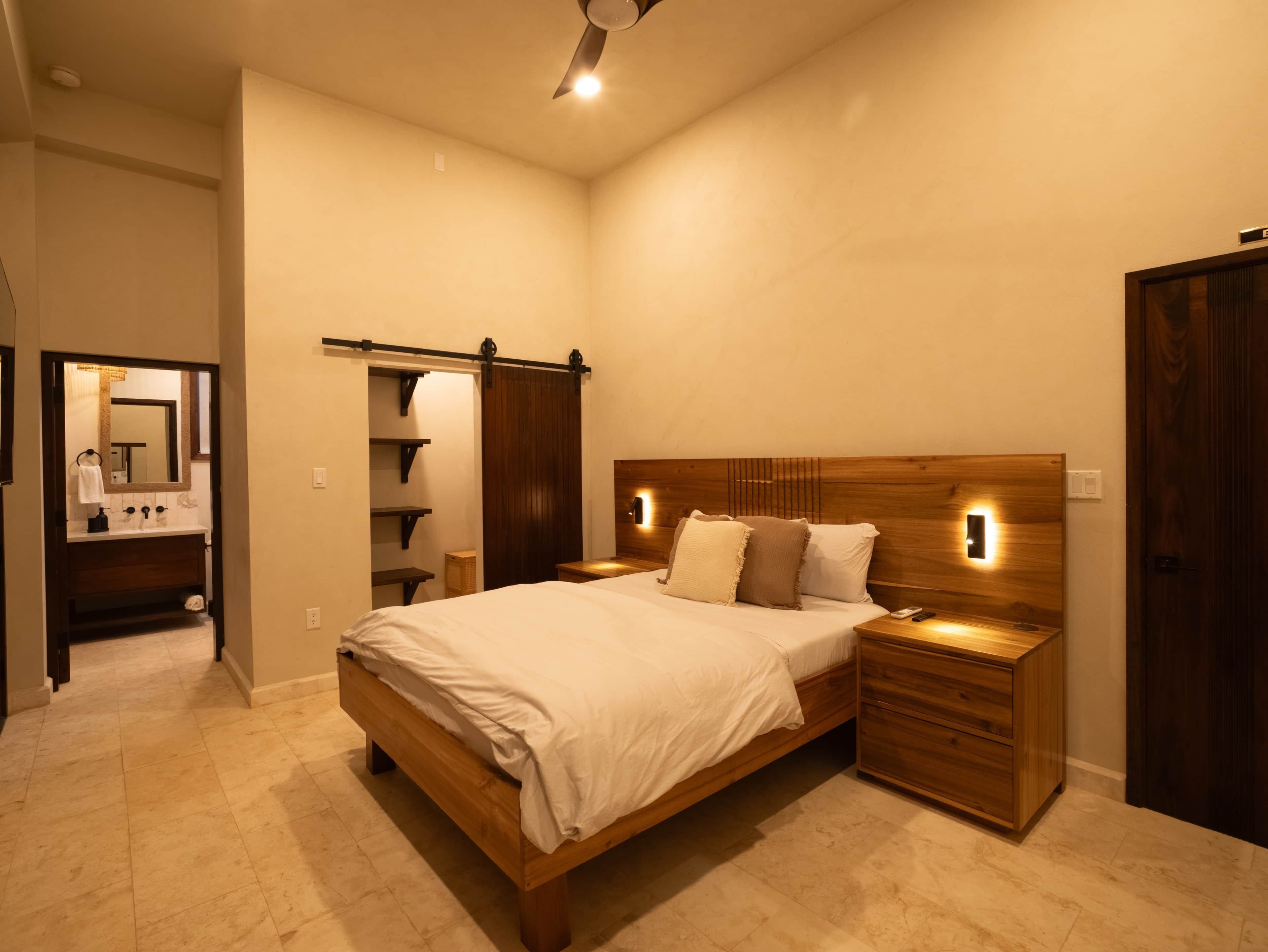 Un dormitorio con cama de madera, mesitas de noche, un tocador, un espejo y un armario.