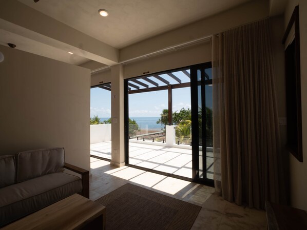 Una sala de estar moderna con un sofá, una mesa de centro y un amplio ventanal corredero que da a un balcón con vistas al mar.
