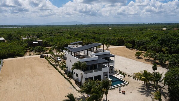 Un edificio moderno a più piani con piscina, circondato da spiaggia sabbiosa e vegetazione.
