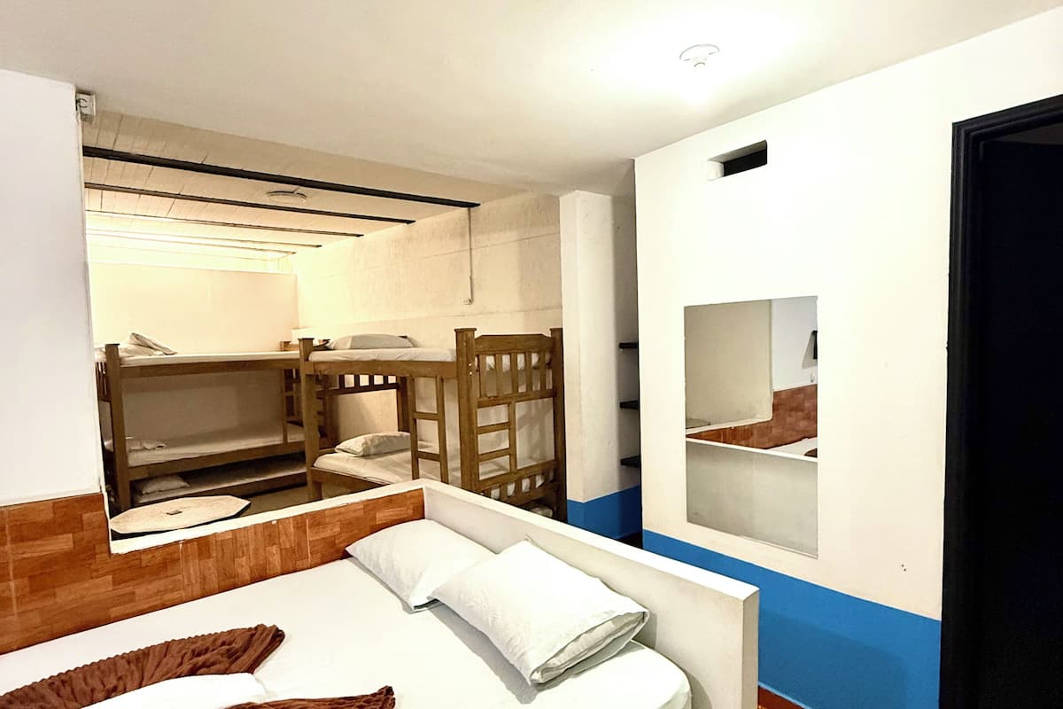 A hotel room with a bed, a mirror, a small seating area, and a bathroom visible through an open door.