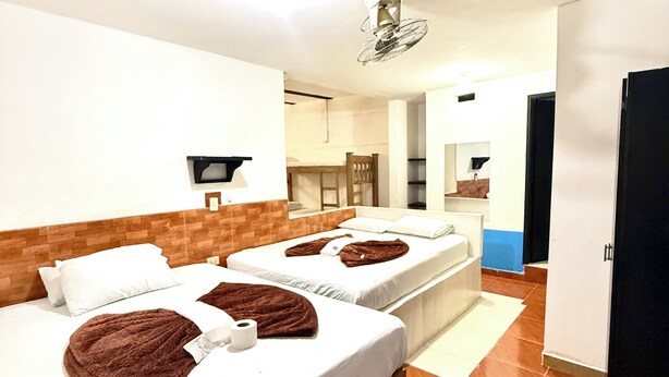 Ein Hotelzimmer mit zwei Betten, einem Deckenventilator, einem kleinen Tisch und einem im Hintergrund sichtbaren Badezimmer.
