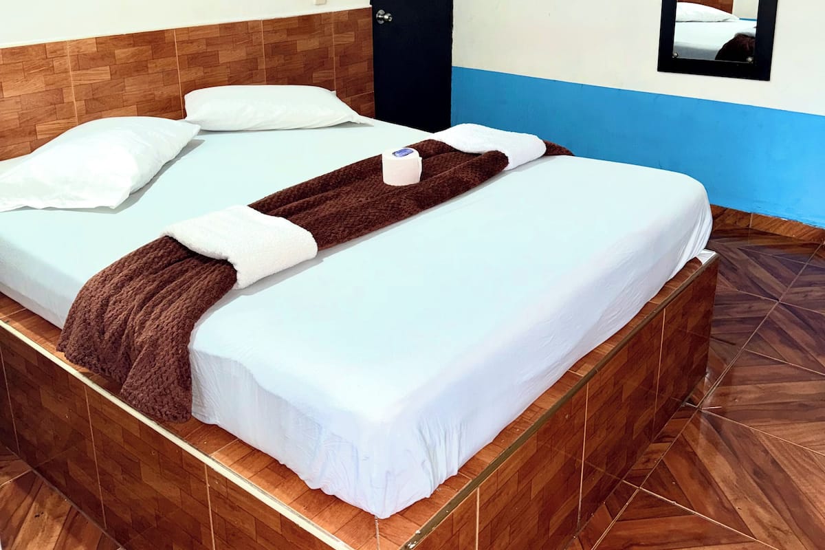 A hotel room with a wooden headboard, a bed with white linens, a brown throw blanket, a black door, and a mirror on the wall.