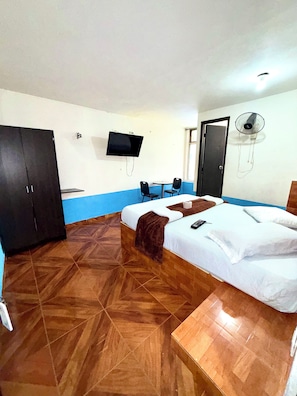 Ein Hotelzimmer mit einem Bett, einem Schreibtisch, einem Sessel, einem Fernseher und einem Ventilator.