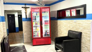 Eine Lobby mit einer Rezeption, zwei roten Coca-Cola-Kühlschränken, schwarzen Ledersitzmöbeln, einem Deckenventilator und einem gefliesten Boden.