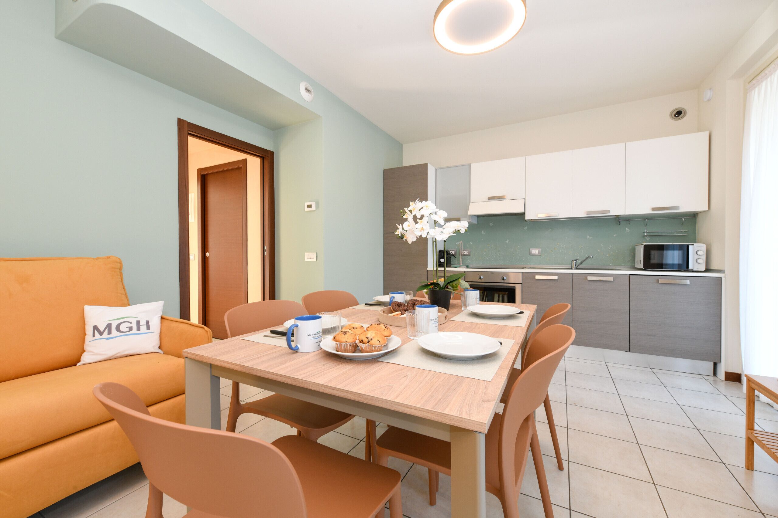 Eine moderne Küche mit Esstisch, Stühlen und einer Couch in einem hellen Raum mit hellblauen Wänden.