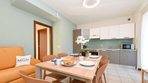 A modern kitchen with a dining table, chairs, and a sofa in a well-lit room with light blue walls. - My Peschiera Holiday Apartment- Quadrivium 4 (Castelnuovo del Garda)
