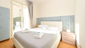 A bedroom with a bed, a nightstand, a window with curtains, and a view of the outdoors. - My Peschiera Holiday Apartment- Quadrivium 4 (Castelnuovo del Garda)