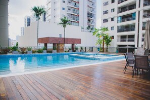 Ein Pool auf dem Dach mit Holzterrasse, umgeben von Hochhäusern und Palmen.