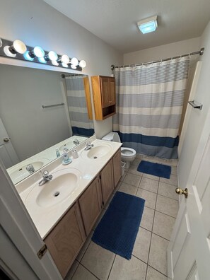 Ein Badezimmer mit zwei Waschbecken, einem Spiegel, einer Toilette, einer Duschvorhang und einer blauen Matte.