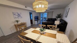 Un coin repas avec une table en bois, des chaises, un lustre et une vue sur le salon.