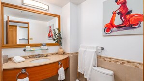 Een badkamer met een wastafel, spiegel, toilet en een schilderij van een rode scooter.