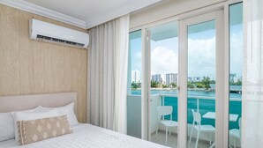 Een hotelkamer met een bed, een airconditioning en uitzicht op zee en stadsgezicht door grote schuifdeuren.