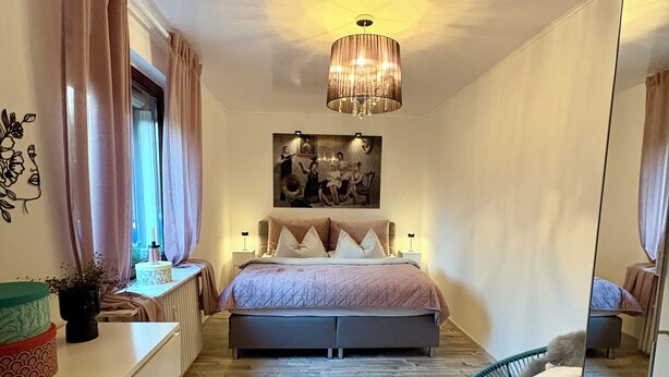 A bedroom with a bed, bedside tables, a mirror, a hanging light fixture, and a window with curtains. - Vacation apartment Seelenglück with garden 🪴🦮 (Bad Harzburg)