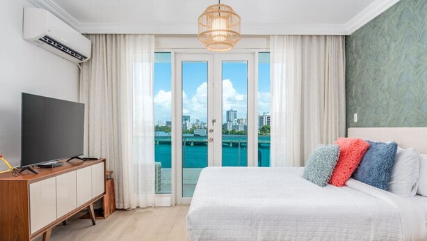A hotel room with a bed, a TV, a wooden cabinet, and a view of a body of water. - Lagoon Studio · Pool & Hot Tub (San Juan)
