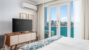 A hotel room with a bed, a TV, a wooden cabinet, and a balcony with a city view. - Waterfront Studio · Pool · Water Backup (San Juan)