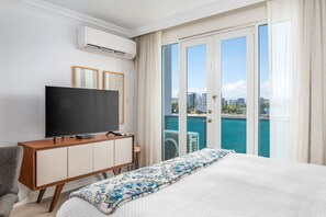Una habitación de hotel con cama, televisión, mueble de madera y balcón con vistas a la ciudad.