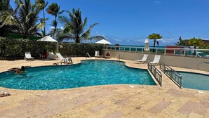 A swimming pool with lounge chairs and umbrellas, surrounded by palm trees and a clear sky. - Waterfront Studio · Pool · Water Backup (San Juan)