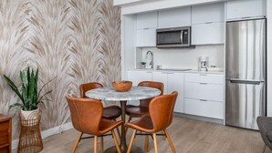 A modern kitchen with white cabinets, a stainless steel refrigerator, a microwave, and a round marble table with leather chairs. - Waterfront Studio · Pool · Water Backup (San Juan)