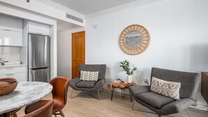 A modern kitchen with a stainless steel refrigerator, a dining table with chairs, and a seating area with two grey armchairs and a small side table with a plant. - Waterfront Studio · Pool · Water Backup (San Juan)