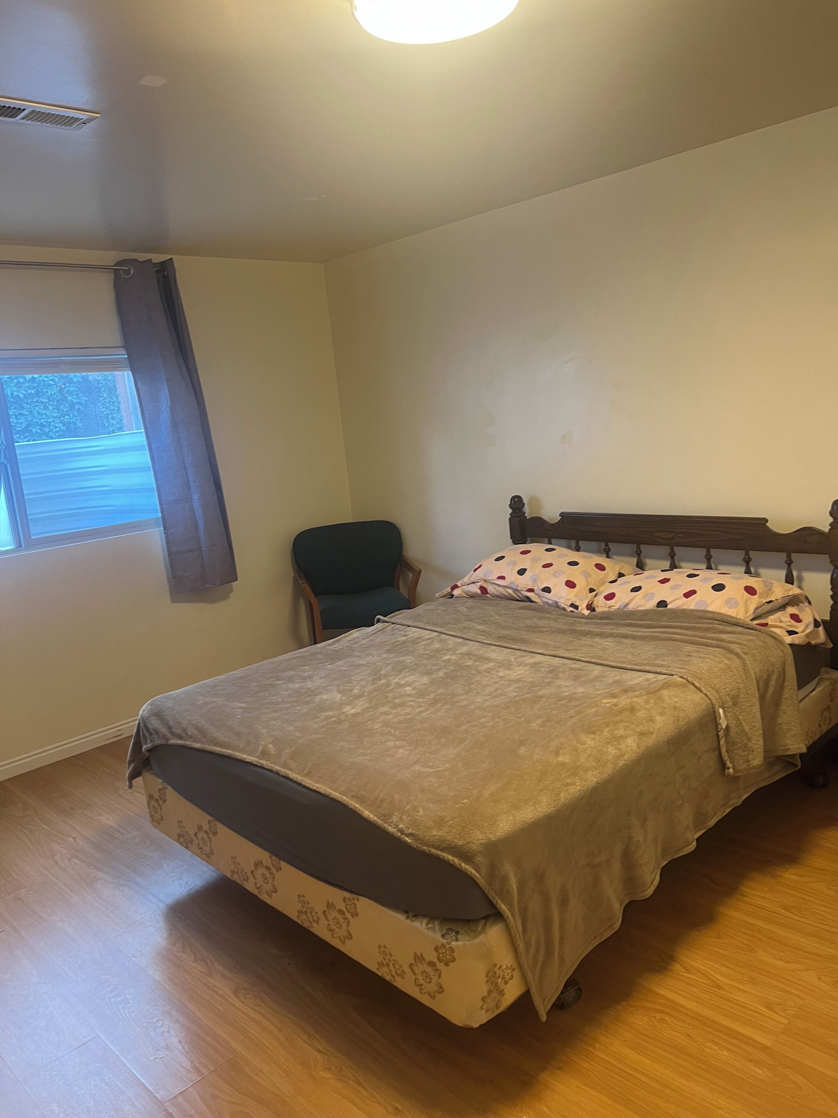 Un dormitorio con cama, una silla, ventana con cortinas y una lámpara de techo.
