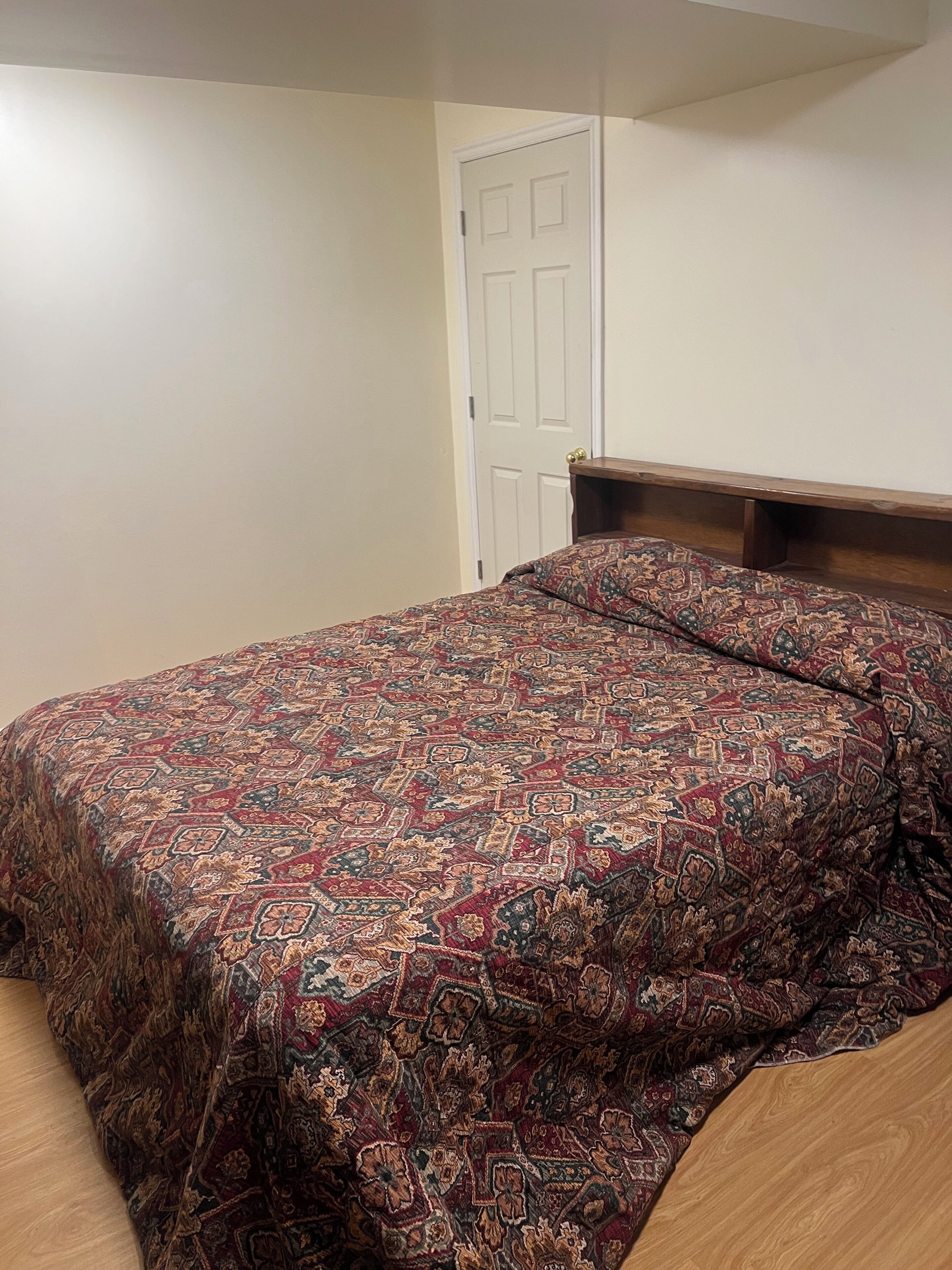 Un dormitorio con cabecera de madera, colcha estampada y una puerta blanca al fondo.