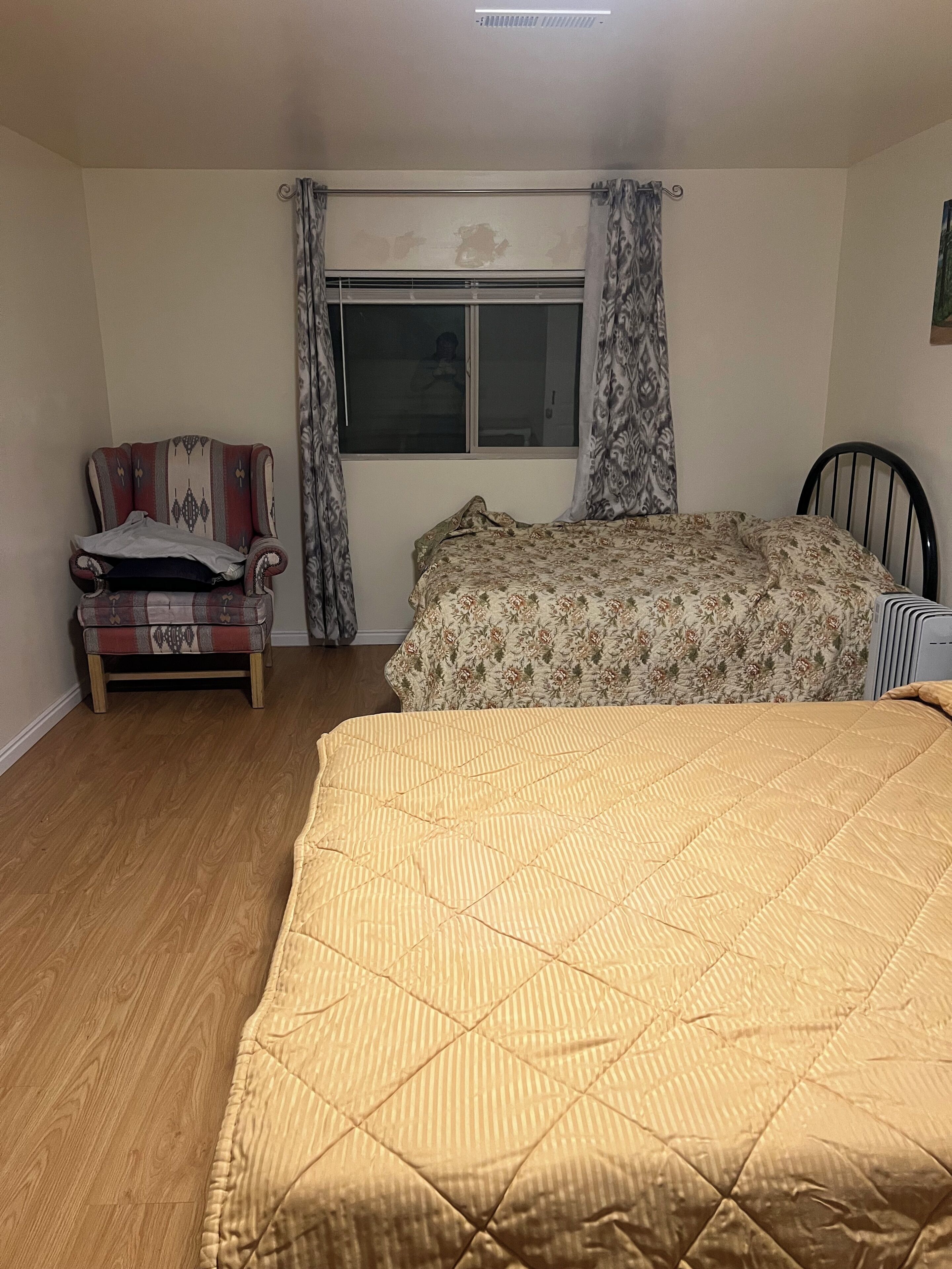 A bedroom with a bed, a chair, a window, and a radiator.