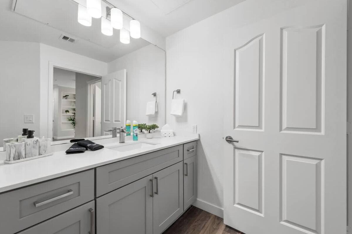 Un baño moderno con un tocador blanco, un espejo grande y una puerta con paneles.