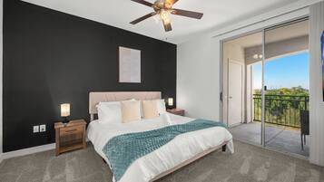 A bedroom with a bed, bedside tables, a ceiling fan, a large window, and a balcony.
