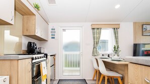 A compact kitchen with a stove, oven, and dining area with chairs and a table. - Seton Sands 3BR Premium Caravan - Near Edinburgh (Port Seton)