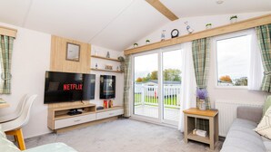 A living room with a TV, sofa, and a sliding glass door leading to a balcony. - Seton Sands 3BR Premium Caravan - Near Edinburgh (Port Seton)