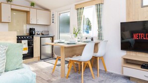 A compact living space with a kitchenette, dining area, and a TV screen displaying 'NETFLIX.' - Seton Sands 3BR Premium Caravan - Near Edinburgh (Port Seton)
