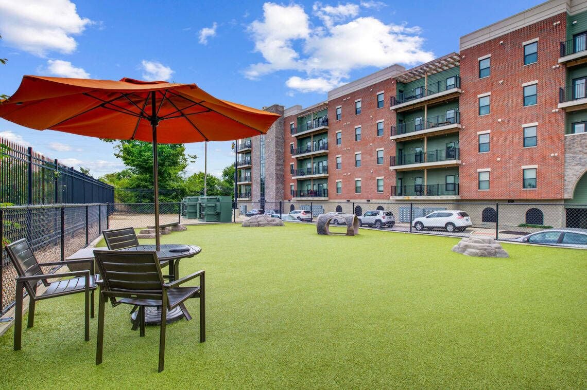 Een binnenplaats met een eettafel en stoelen, een rode parasol en een bakstenen gebouw met balkons.