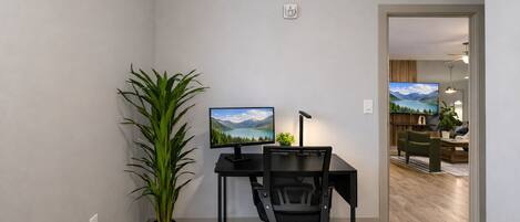 A modern office space with a desk, chair, computer monitor, and a potted plant.