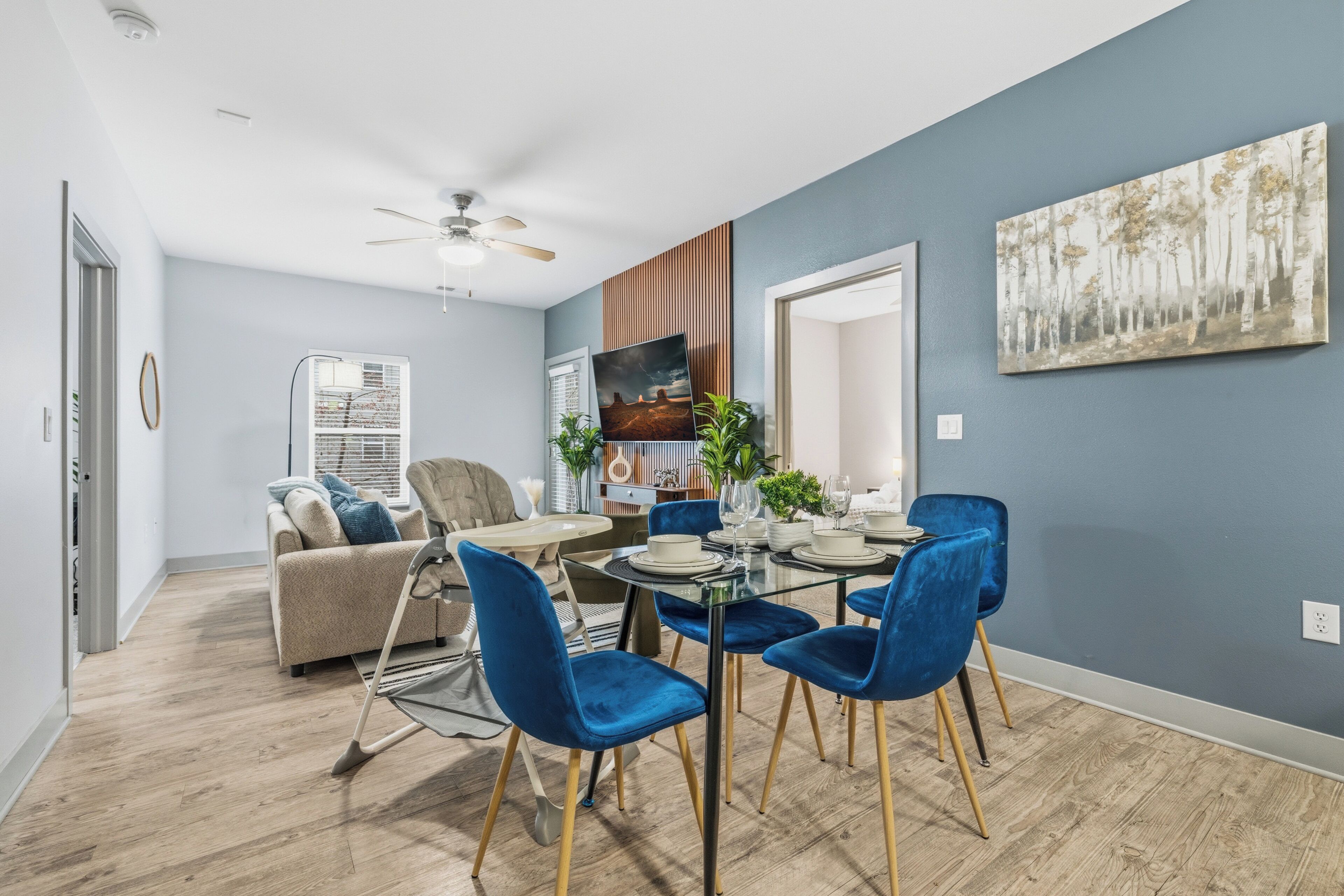 Un salon moderne comprenant un coin repas, un ventilateur de plafond, une grande fenêtre et un tableau au mur.