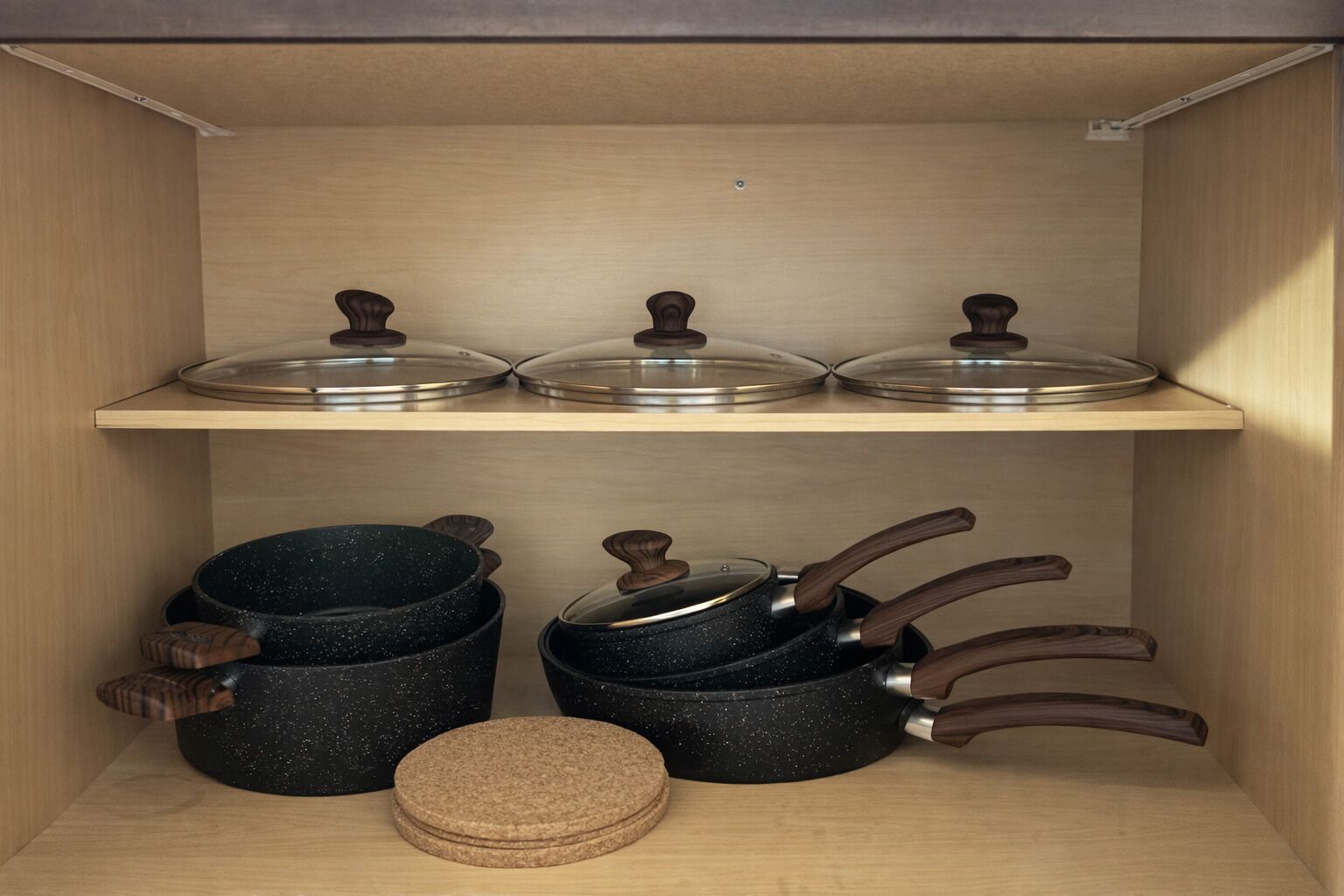 Une étagère de cuisine avec trois pots et leurs couvercles, ainsi qu’un ensemble de dessous de verre.