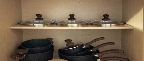 Une étagère de cuisine avec trois pots et leurs couvercles, ainsi qu’un ensemble de dessous de verre.