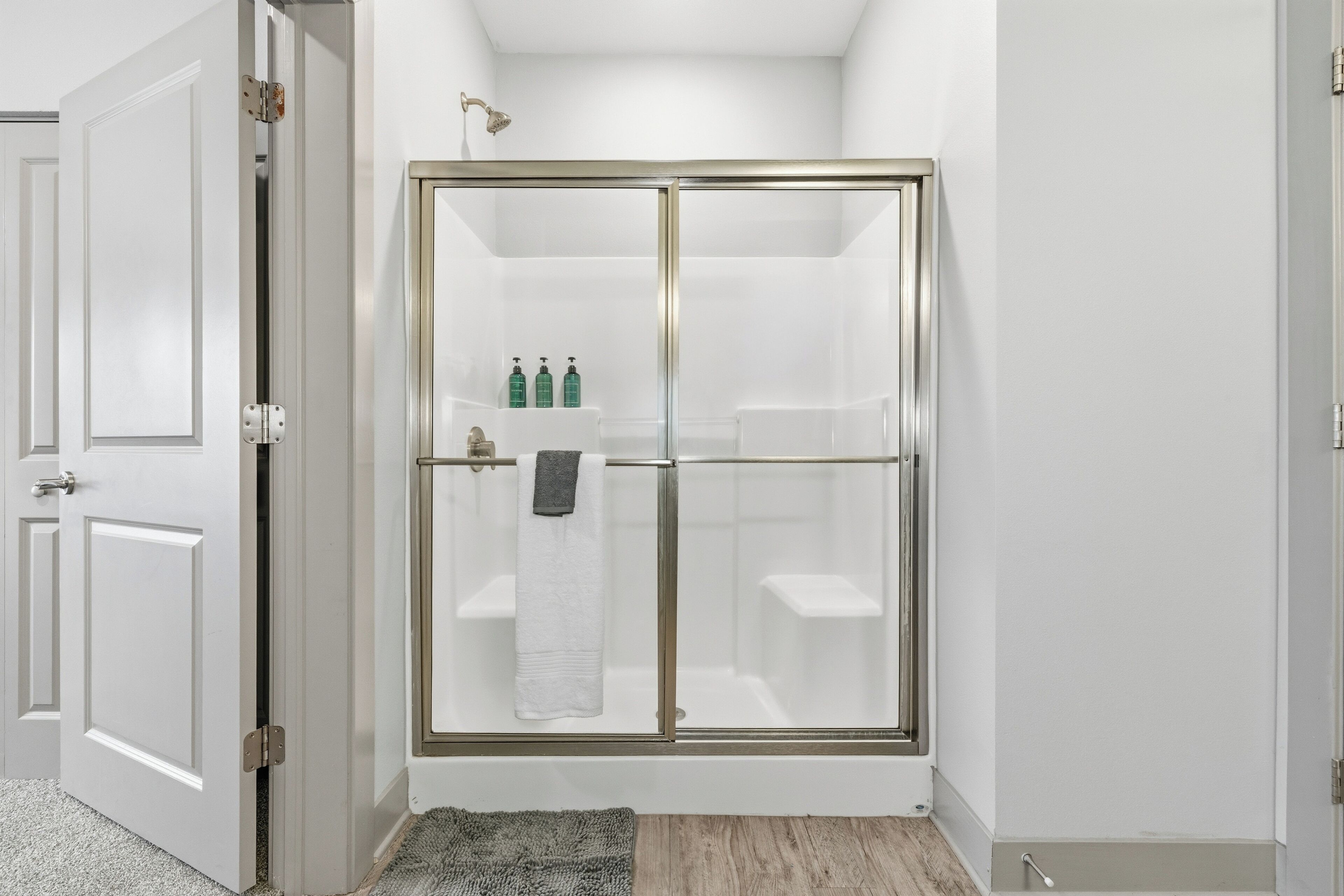 A modern bathroom with a glass shower enclosure, a white towel hanging on the door, and a small shelf with toiletries.