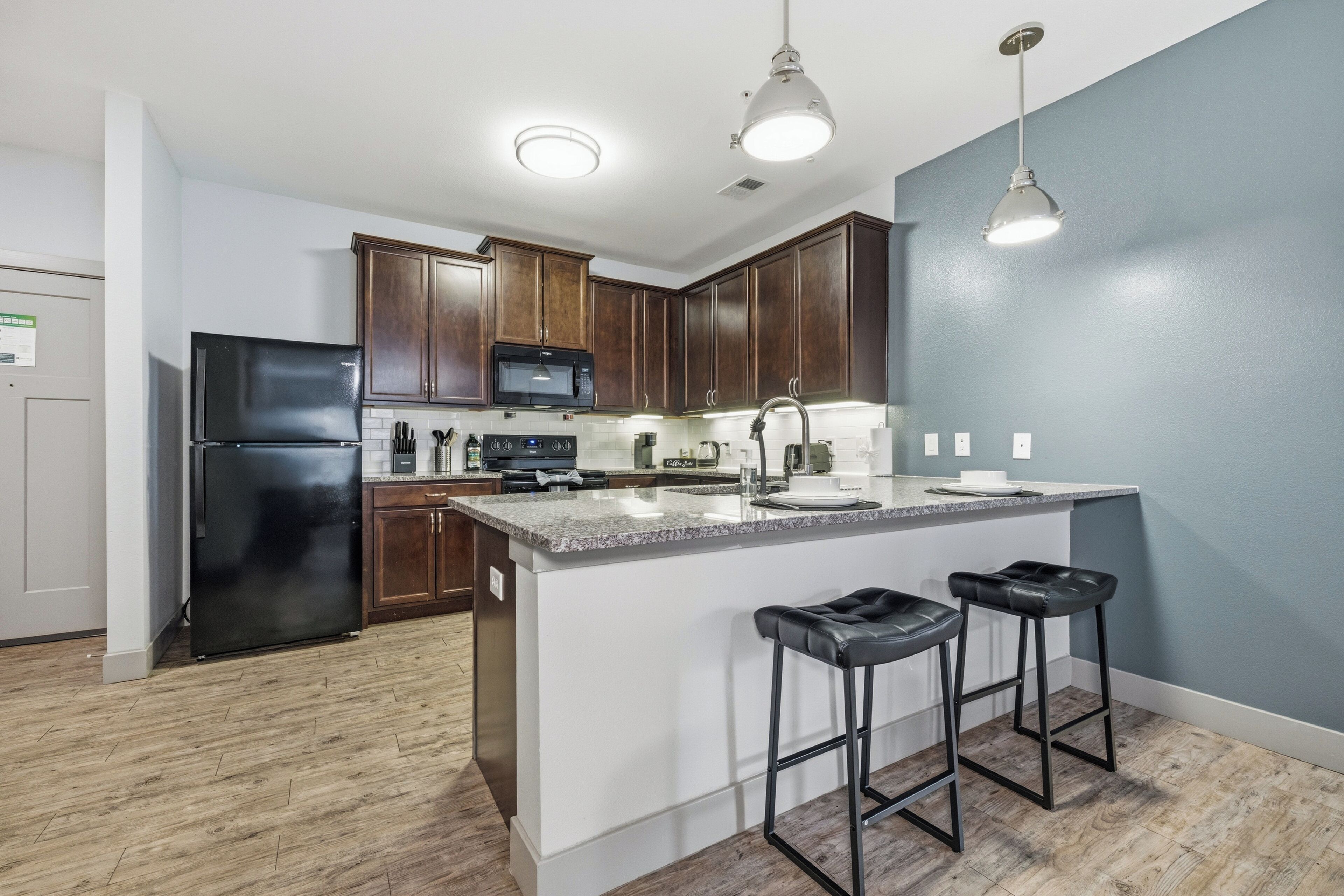 A modern kitchen with dark wooden cabinets, a black refrigerator, a microwave, and a large island with bar stools.