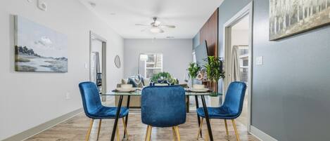 A dining area with a glass table, blue chairs, and a ceiling fan.