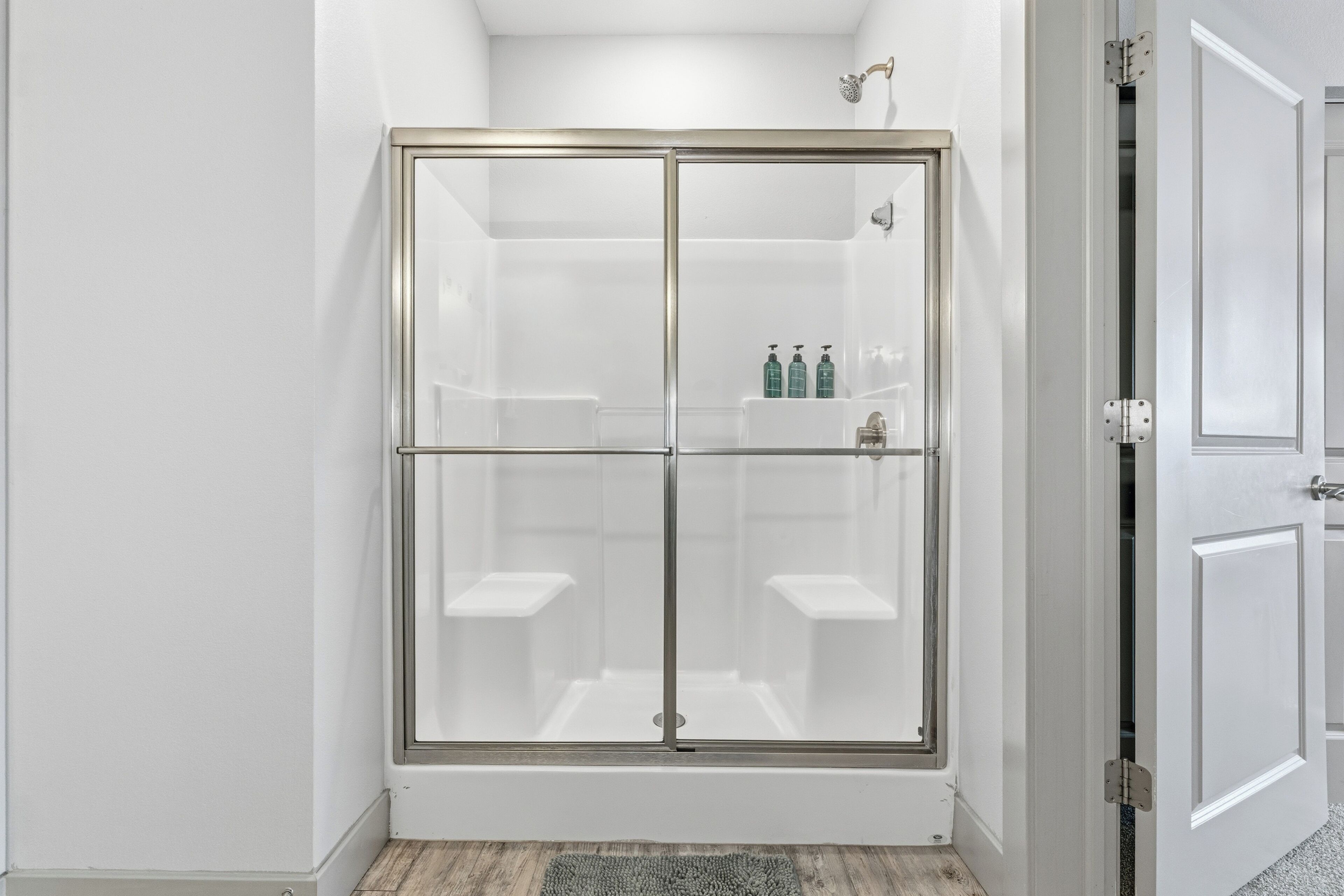 A walk-in shower with a glass door, a white tiled wall, and a small shelf with toiletries.