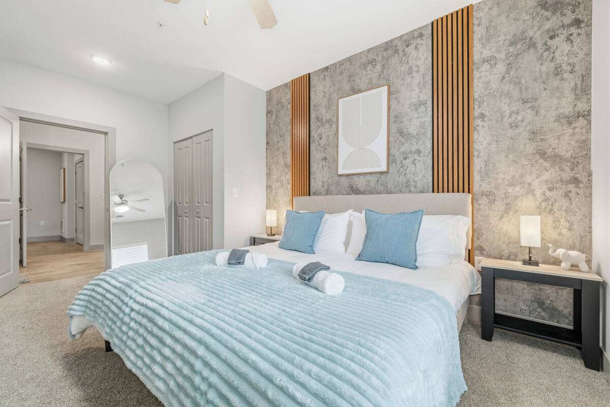 A modern hotel room with a large bed, a wooden accent wall, and a ceiling fan.